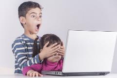 Little boy protects his sister from watching inappropriate content while using a computer. Internet safety for kids concept. Toned image with selective focus